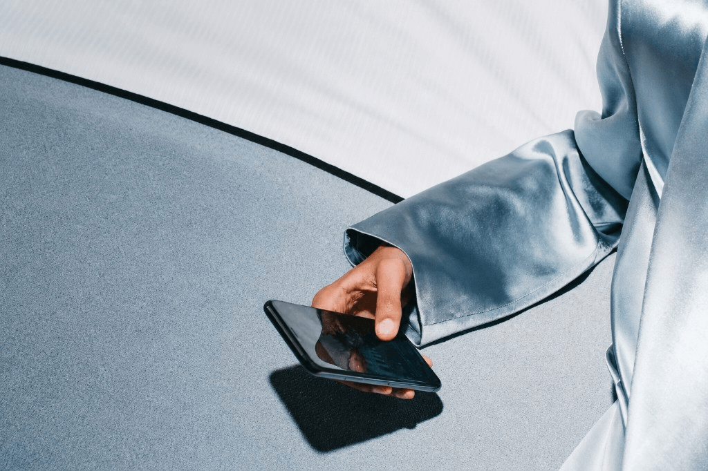 Hand holding smartphone on pale surfaces — partial arm and cuff, commerce in context